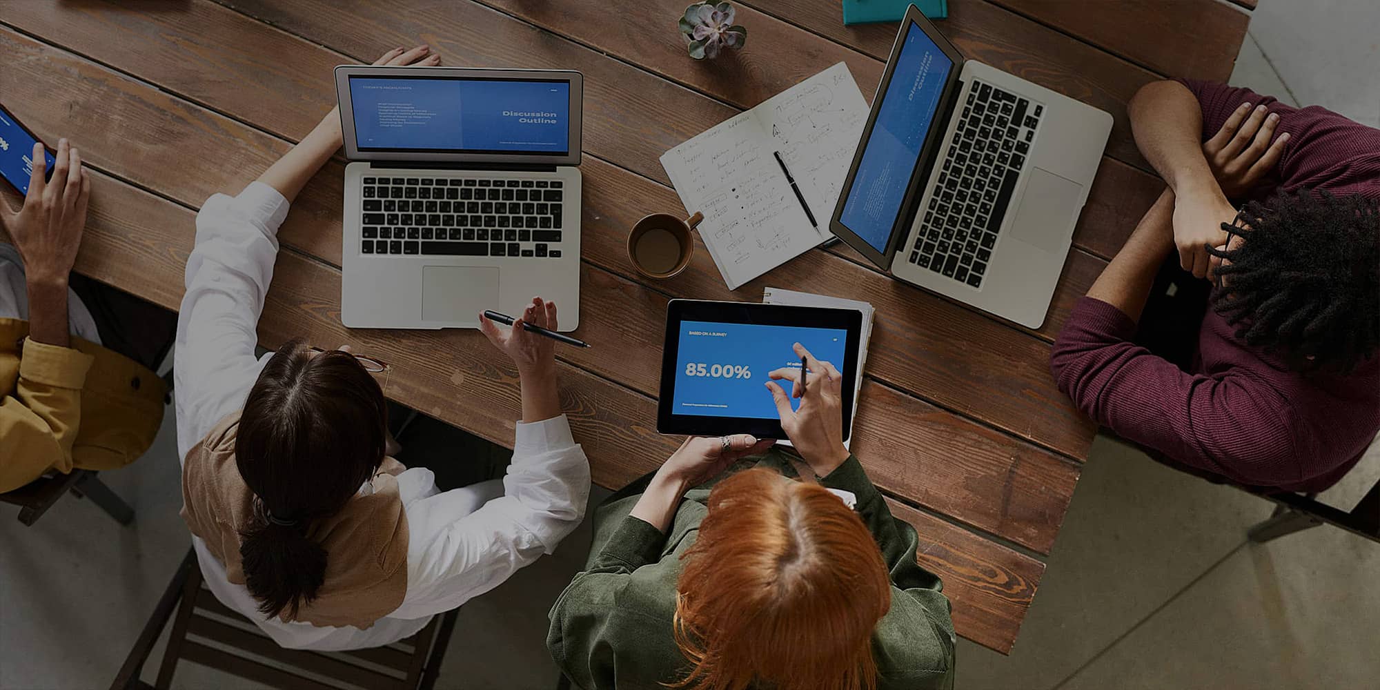 Réunion de travail autour d’une table en bois avec ordinateurs portables et tablette, illustrant la création d’entreprise et la structuration d’un projet professionnel.
