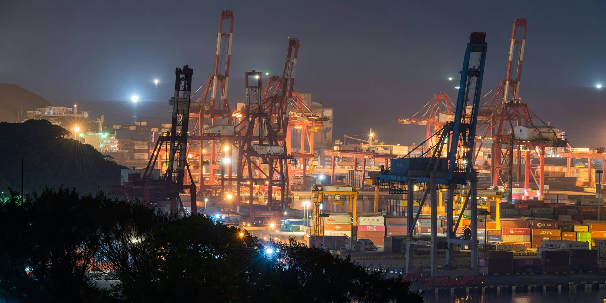Zone portuaire avec grues et installations industrielles de nuit, symbolisant des chantiers d’envergure et l’encadrement contractuel des opérations de travaux et des relations commerciales