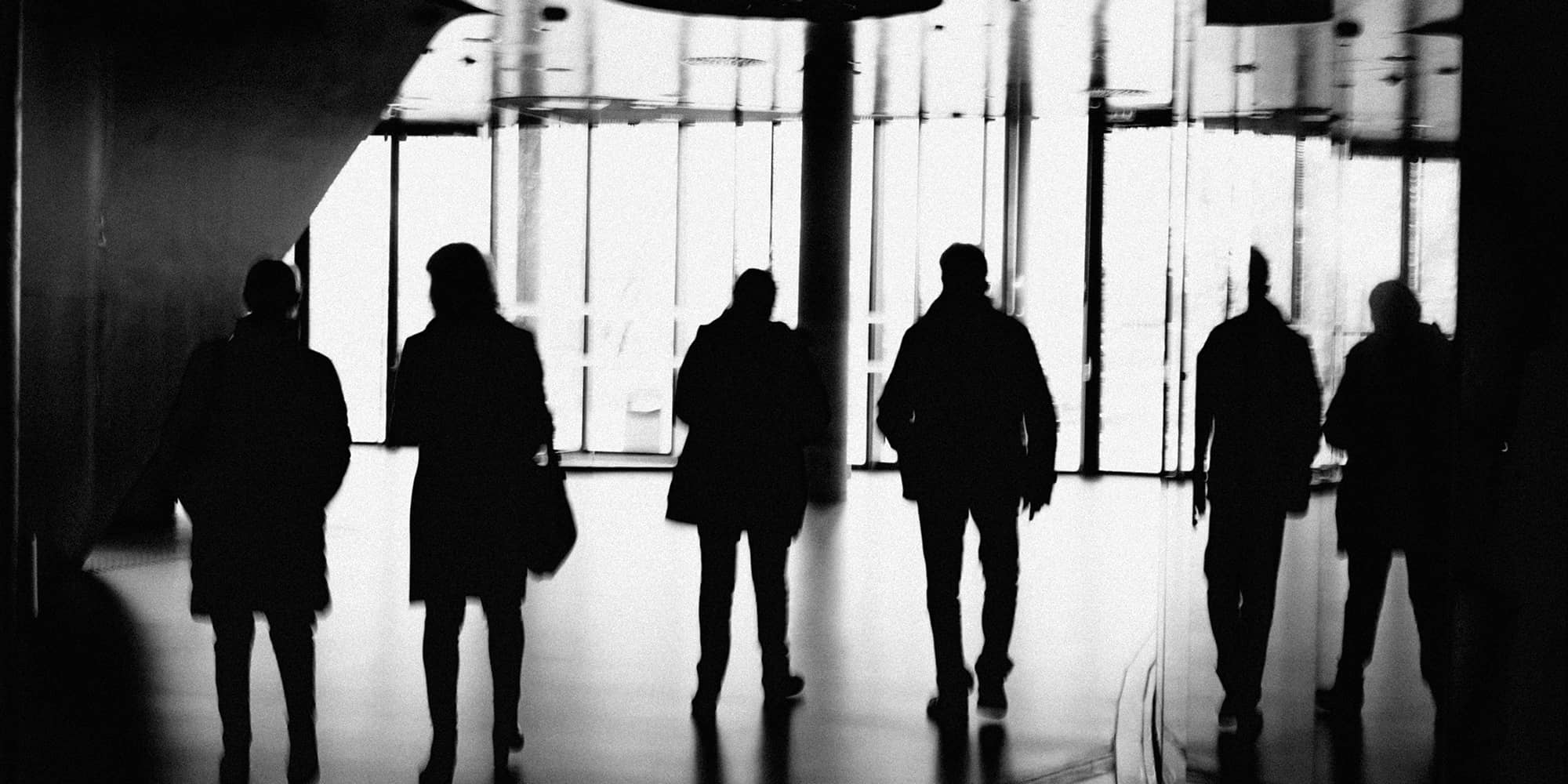 Silhouettes de plusieurs associés se croisant dans un espace professionnel, illustrant une situation de mésentente entre associés