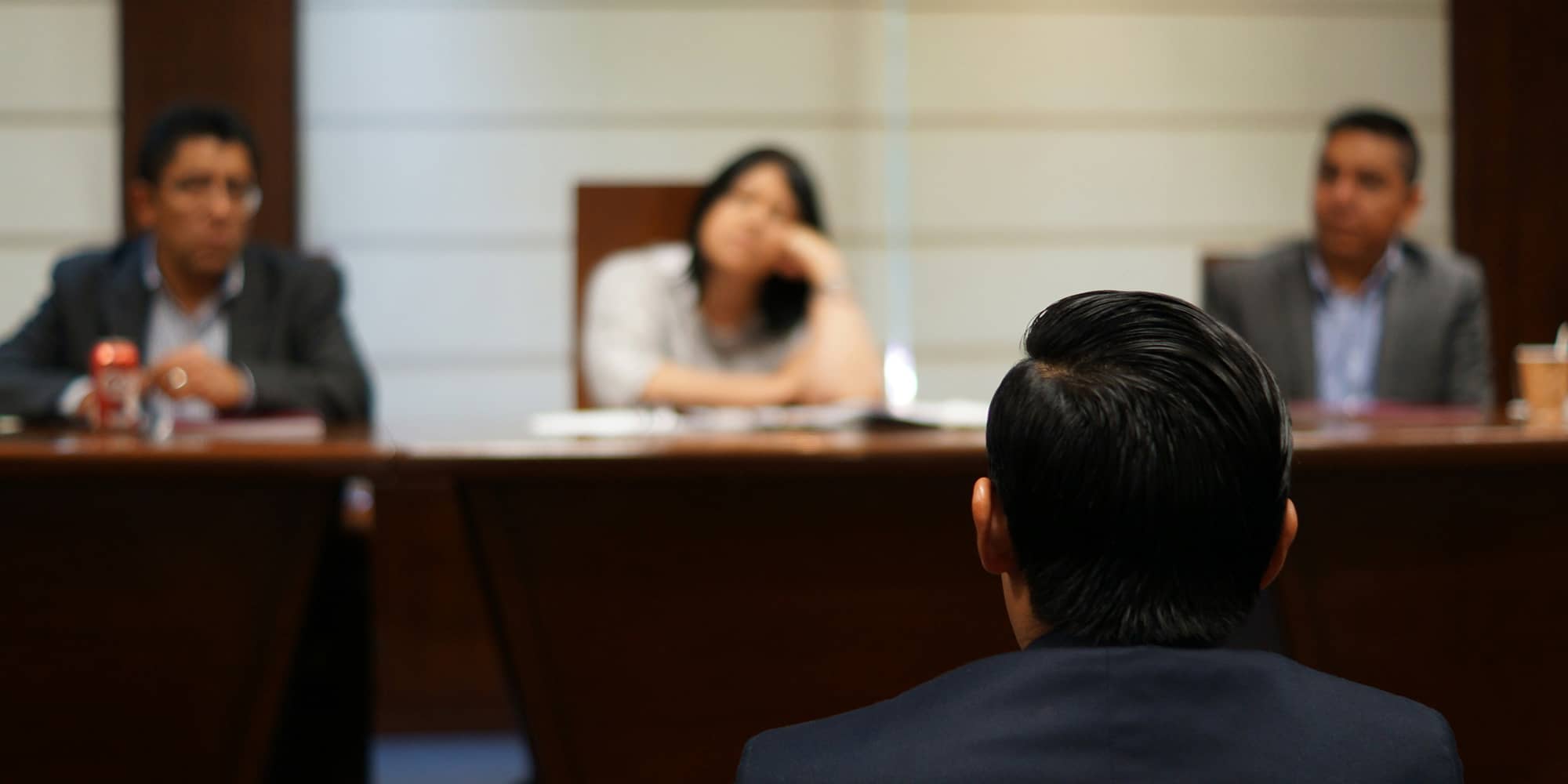 Audience judiciaire : une personne de dos fait face à un tribunal composé de juges assis derrière un bureau, illustrant une procédure de recouvrement judiciaire de créance.